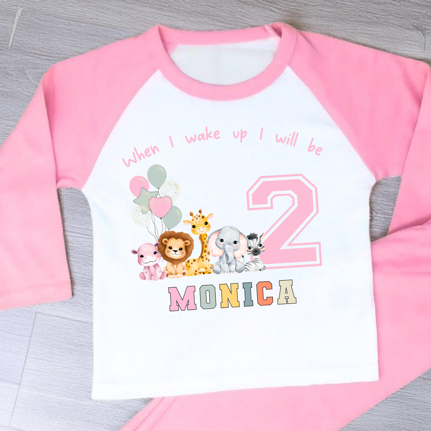 safari birthday pyjamas, A personalised set of girls birthday pyjamas in pink. At the top it says when i wake up i will be followed by some safari jungle animals holding some birthday balloons. They are sat beside a number that represents the child age on birthday. Under that is the child name in safari rainbow colours. This is perfect gift for a toddler first birthday.