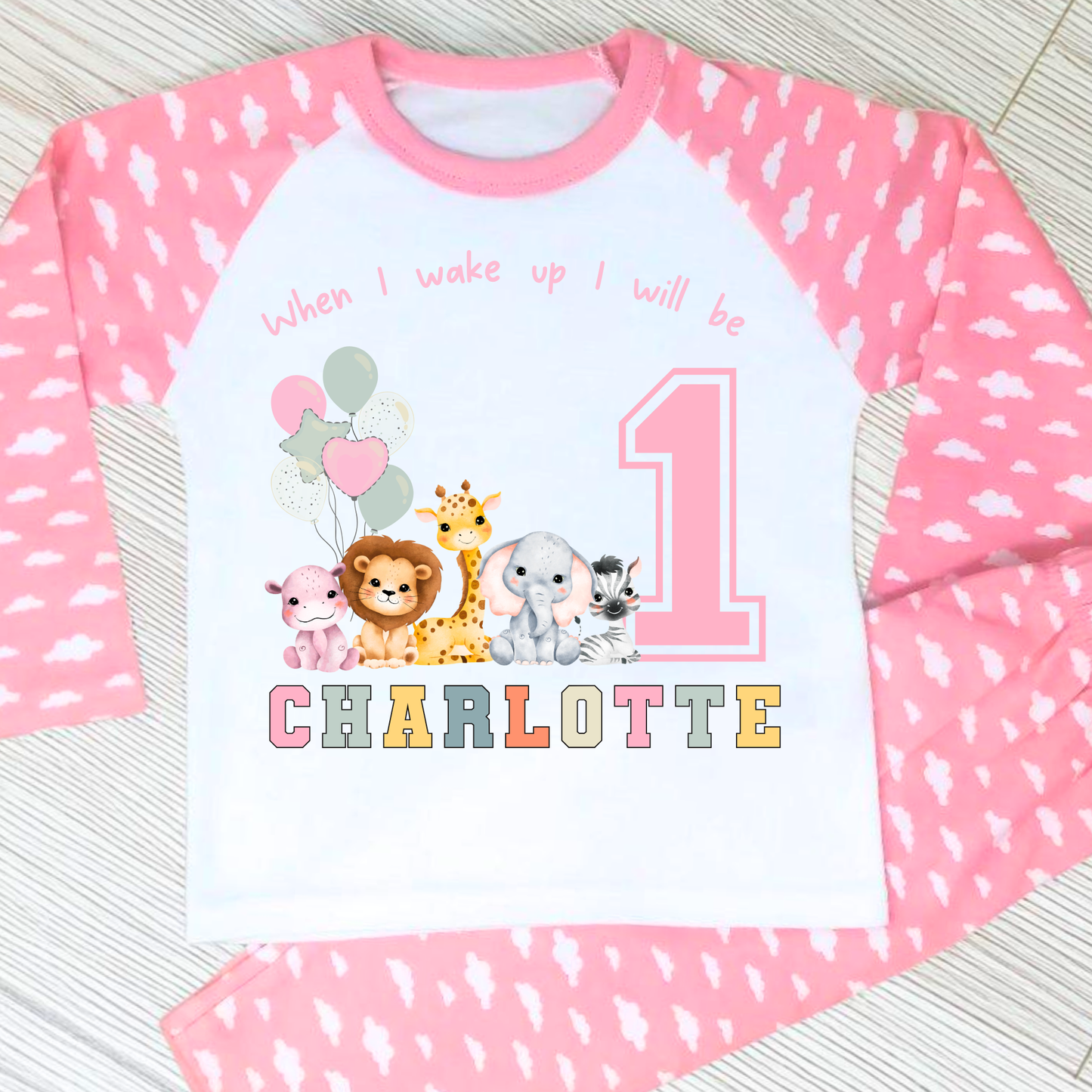 safari birthday pyjamas, A personalised set of girls birthday pyjamas in pink. At the top it says when i wake up i will be followed by some safari jungle animals holding some birthday balloons. They are sat beside a number that represents the child age on birthday. Under that is the child name in safari rainbow colours. This is perfect gift for a toddler first birthday.