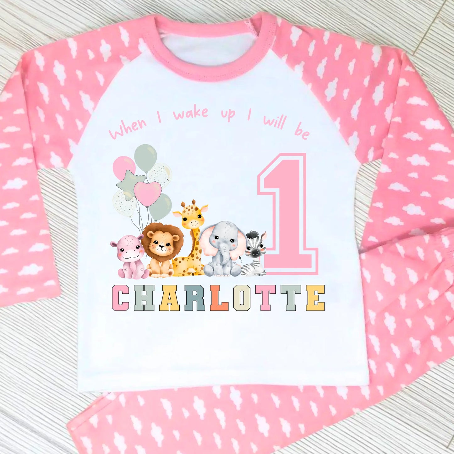 safari birthday pyjamas, A personalised set of girls birthday pyjamas in pink. At the top it says when i wake up i will be followed by some safari jungle animals holding some birthday balloons. They are sat beside a number that represents the child age on birthday. Under that is the child name in safari rainbow colours. This is perfect gift for a toddler first birthday.