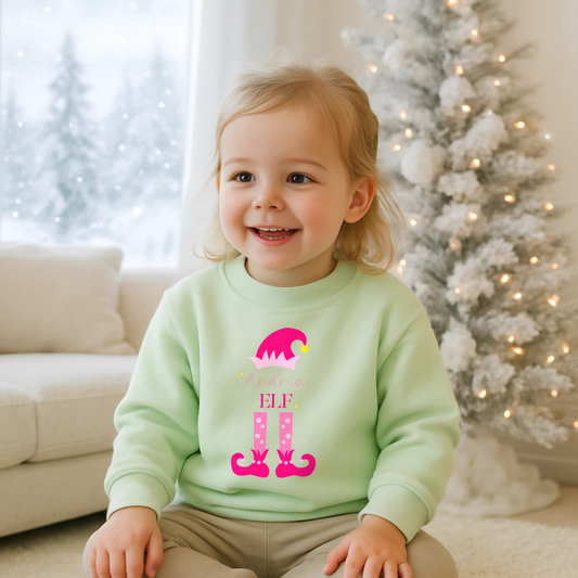 Personalised christmas elf sweatshirt: A pink sweatshirt featuring a cute elf design. It’s personalised with a child's name, adding a special touch to the festive season. Made from soft, high-quality materials for comfort and warmth. Ideal for Christmas gatherings and events, particularly Christmas jumper day