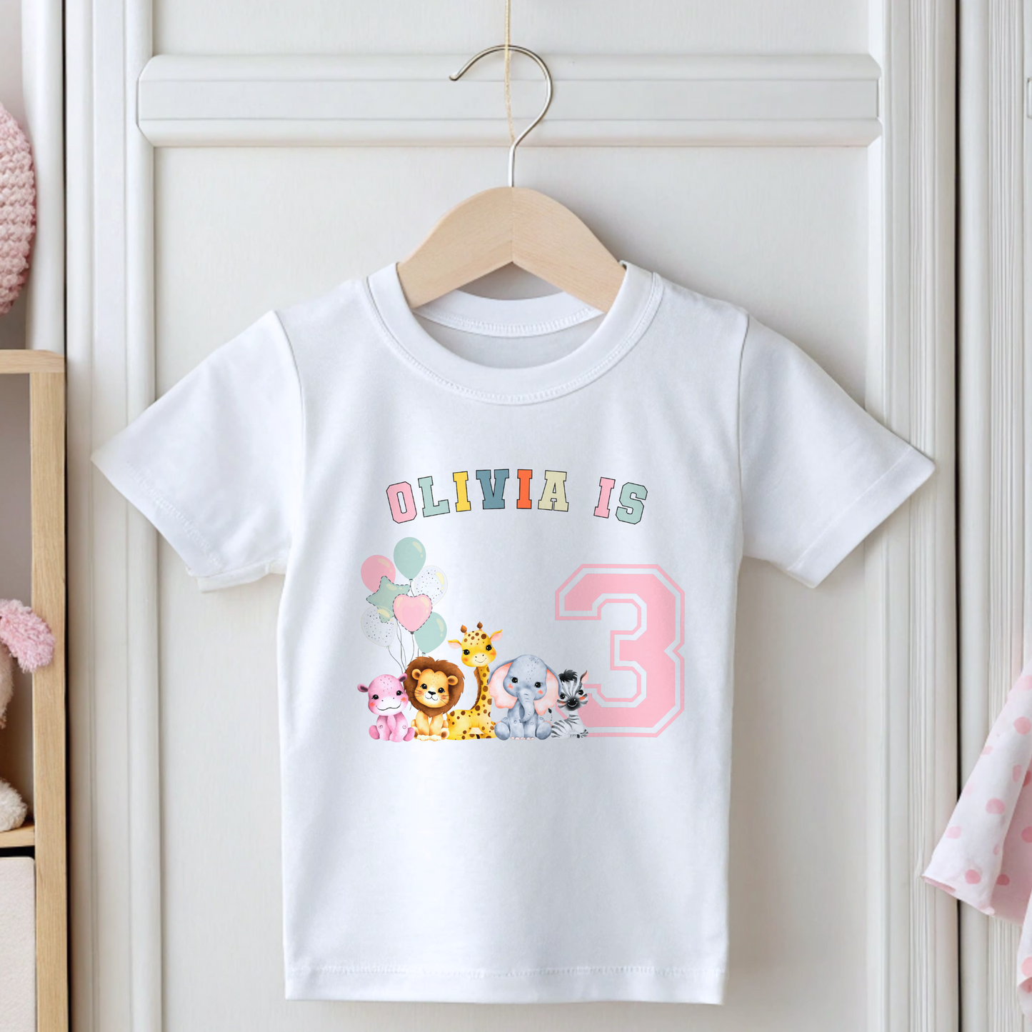 Animal birthday t-shirt, A white t-shirt featuring a vibrant graphic with pink, sage, and neutral tones, showcasing a personalized "Birthday Girl" design. The graphic includes the girl's name and an age-representing number. It incorporates a lively safari jungle animal theme adorned with colorful birthday balloons. This t-shirt makes an ideal birthday gift for a toddler safari-themed birthday party celebration, adding a personalized touch to the festivities.