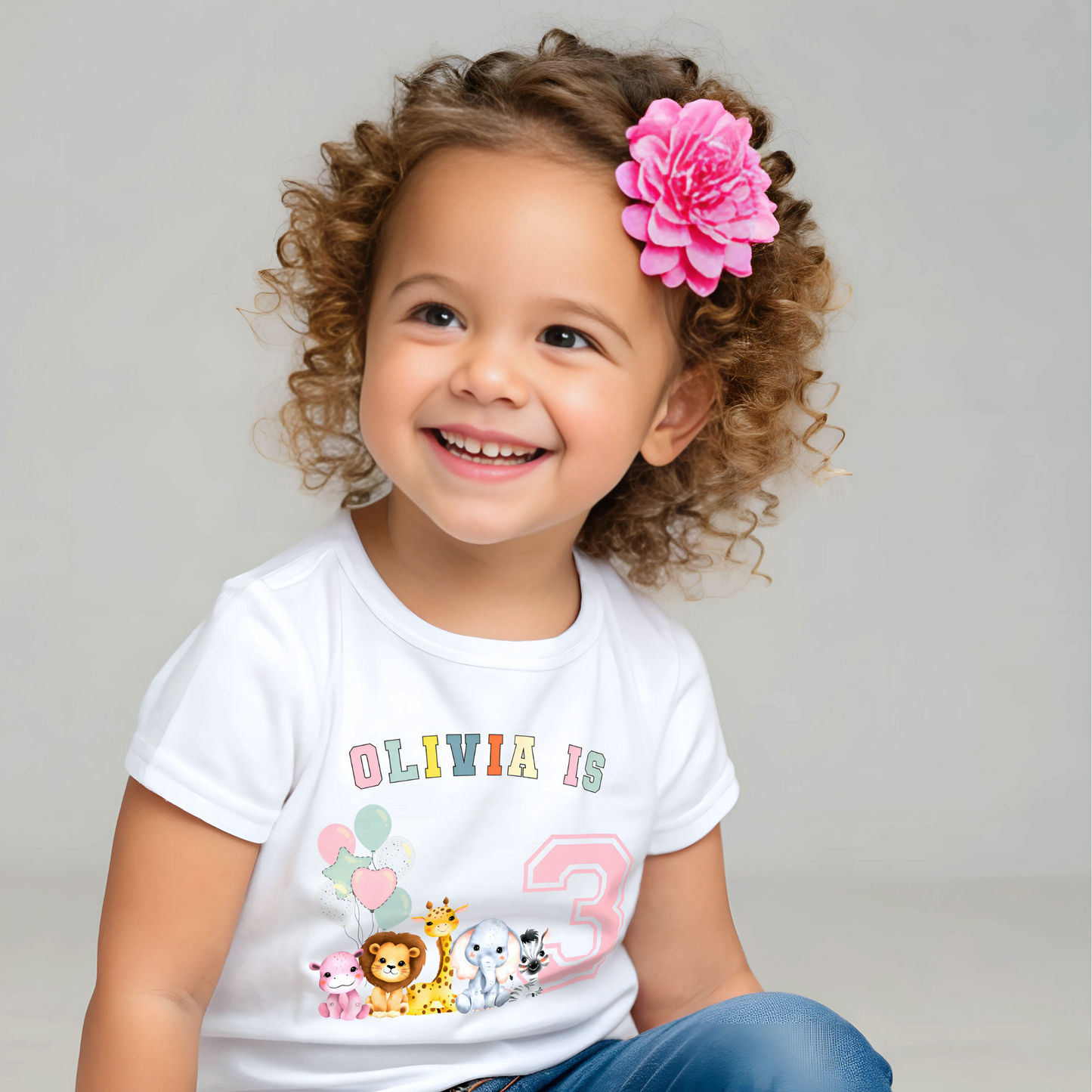 Animal birthday t-shirt, A white t-shirt featuring a vibrant graphic with pink, sage, and neutral tones, showcasing a personalized "Birthday Girl" design. The graphic includes the girl's name and an age-representing number. It incorporates a lively safari jungle animal theme adorned with colorful birthday balloons. This t-shirt makes an ideal birthday gift for a toddler safari-themed birthday party celebration, adding a personalized touch to the festivities.