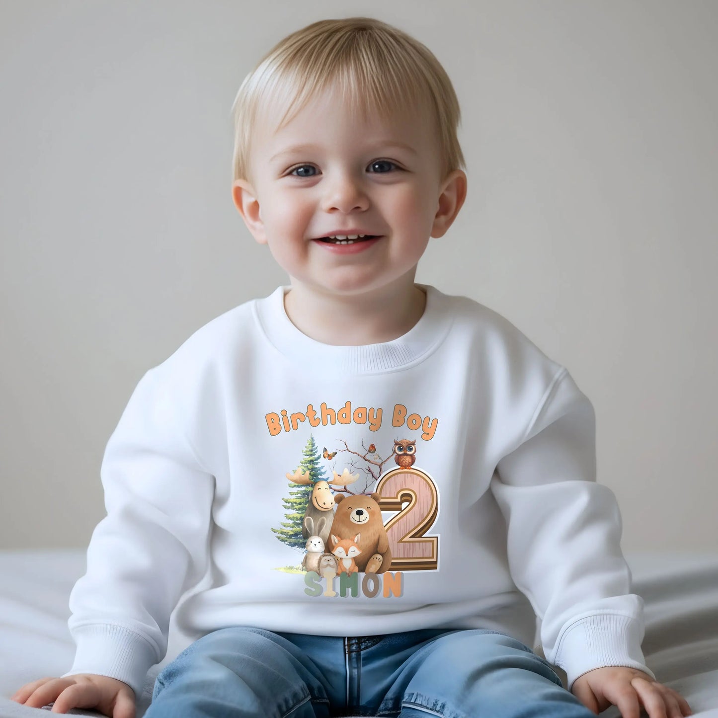 Woodland animal birthday sweatshirt: A children's birthday jumper featuring a woodland animal theme. The shirt displays a forest scene with a playful fox, a curious bear, and a gentle bear, surrounded by lush greenery. The design uses earthy tones and vibrant greens to create a natural look. At the top, the words “Birthday Boy” are printed, with space for a personalized name underneath.