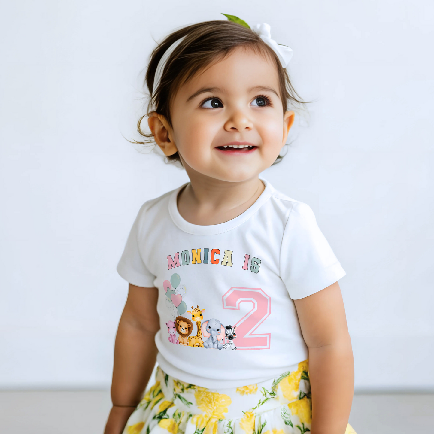 Animal birthday t-shirt, A white t-shirt featuring a vibrant graphic with pink, sage, and neutral tones, showcasing a personalized "Birthday Girl" design. The graphic includes the girl's name and an age-representing number. It incorporates a lively safari jungle animal theme adorned with colorful birthday balloons. This t-shirt makes an ideal birthday gift for a toddler safari-themed birthday party celebration, adding a personalized touch to the festivities.