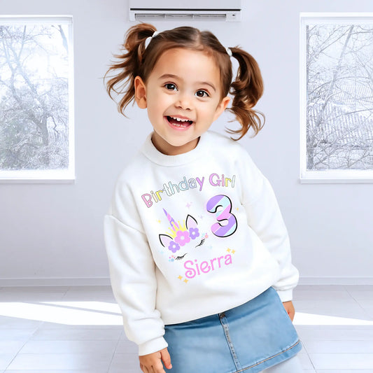Unicorn Birthday Sweatshirt, A personalised birthday jumper for girls, featuring a pink and purple unicorn design. The sweatshirt is customisable with the child's name and age, making it a perfect birthday gift. The vibrant colours and whimsical unicorn imagery make it an ideal choice for a toddler celebrating her special day.