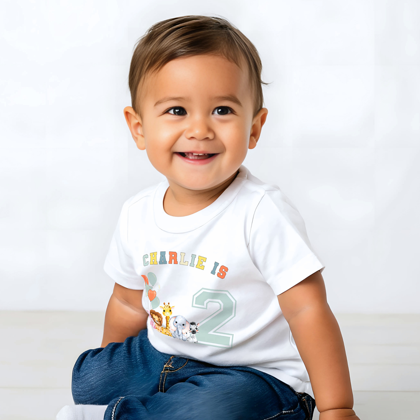 Animal birthday t-shirt, A white t-shirt featuring a vibrant graphic with sage, and neutral tones, showcasing a personalized birthday boy design. The graphic includes the boys name and an age-representing number. It incorporates a lively safari jungle animal theme adorned with colourful birthday balloons. This t-shirt makes an ideal birthday gift for a toddler safari-themed birthday party celebration, adding a personalised touch to the festivities.