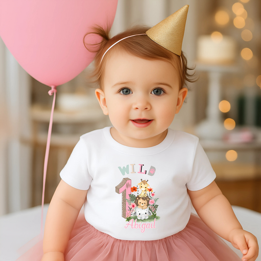 Wild One birthday t-shirt: A personalised Wild One 1st Birthday T-shirt for girls, featuring charming safari animals and vibrant colours. The shirt, designed for a jungle safari theme birthdays, includes space to customise with your child's name. Made from soft, high-quality materials, it promises comfort and style for your baby's first birthday celebration.