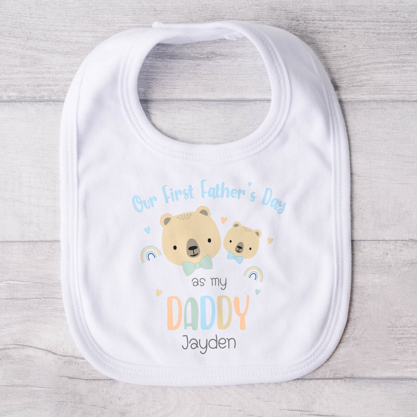 First Father's Day Outfit: A baby dressed in a personalized First Father’s Day outfit. This unique gift for new dads includes a choice of a sleepsuit, vest, T-shirt, or bib, all featuring a charming design. At the top, it reads “First Father’s Day as My Daddy,” accompanied by an adorable illustration of a baby bear and a father bear, along with the child’s name.