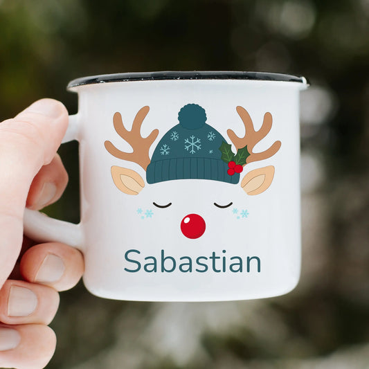 kids christmas mug: Personalised Christmas Mug with a reindeer design and 'Sabastian' text, held by a hand against a blurred natural background.