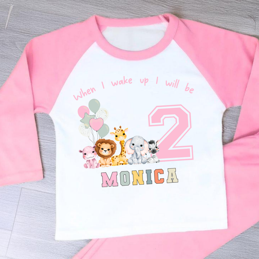 safari birthday pyjamas, A personalised set of girls birthday pyjamas in pink. At the top it says when i wake up i will be followed by some safari jungle animals holding some birthday balloons. They are sat beside a number that represents the child age on birthday. Under that is the child name in safari rainbow colours. This is perfect gift for a toddler first birthday.