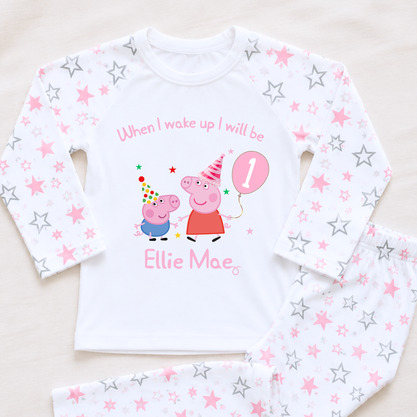 Girls Personalised Peppa and George Pig Birthday Pyjamas, Peppa Pig birthday pyjamas, Peppa Pig Personalised Pyjamas, When I wake Up I'll Be Pj's, Girls Peppa Pig Pjs, Peppa Pig Birthday Gift, Name Pyjamas, Happy Birthday Pjs, A children's long-sleeve pajama set laid flat on a light beige surface. The white pajama top has an all-over pink and silver star print and a central Peppa Pig birthday graphic with the text 'When I wake up up I will be' and 'Ellie Mae' with a pink balloon showing the number 1.