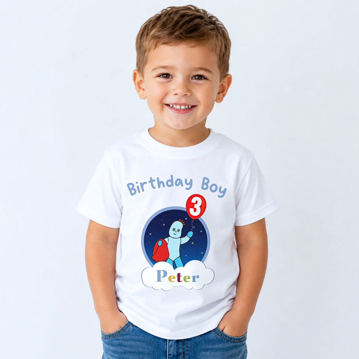 A smiling young boy wearing a white personalised t-shirt with a 'Birthday Boy Peter' space-themed graphic, paired with blue jeans, set against a plain light gray background. In the Night Garden theme with Iggle Piggle.