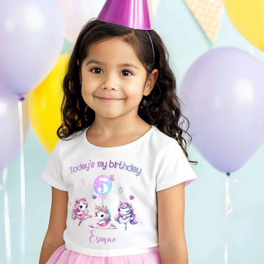 A pastel pink and lilac unicorn birthday T-shirt for girls and toddlers, featuring a cute unicorn design. Made from soft, breathable 100% cotton, this shirt offers both style and comfort. It can be personalised with a name, making it a unique birthday gift for girls. Perfect for a little dancer's birthday celebration, combining magic and comfort as she twirls and plays. Unicorn birthday gift, personalised unicorn, custom name tshirt