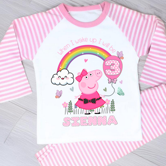 Peppa Pig birthday pyjamas: set of Personalised Peppa Pig Birthday Pyjamas designed for little girls, featuring Peppa Pig in a whimsical spring garden theme with blooming flowers and vibrant colours. The pyjamas include a playful rainbow with pink polka dots, displaying the child's age for a personalised touch. The set is personalised with the child's name, making it a unique gift for Peppa Pig fans, perfect for wearing on the eve of their birthday.