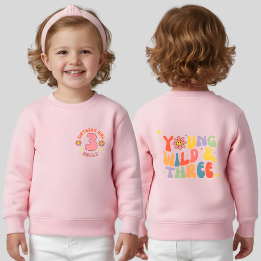 Girls Young Wild and Three birthday sweatshirt in groovy retro style, featuring birthday girl text, retro emojis, a personalised name on the front and bold nostalgic graphics on the back