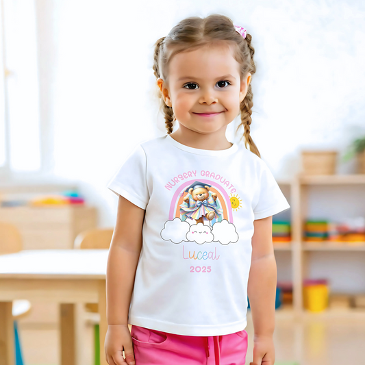 A girl wearing a white Personalised Nursery Leavers T-shirt. Above the rainbow it says Nursery Graduate and below it is a girl bear in graduation clothes on soft fluffy clouds. Below the design is the girls name and year of graduation.