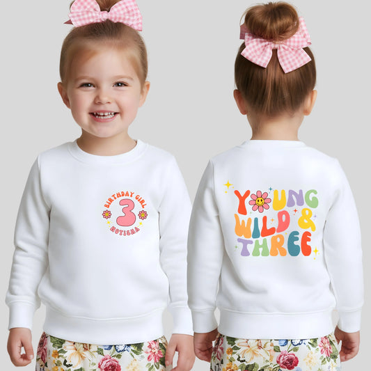 Girls Young Wild and Three birthday sweatshirt in groovy retro style, featuring birthday girl text, retro emojis, a personalised name on the front and bold nostalgic graphics on the back