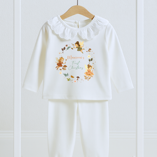 First Christmas Pyjamas: White frill baby pyjamas with floral design and text on a wooden hanger against a white background