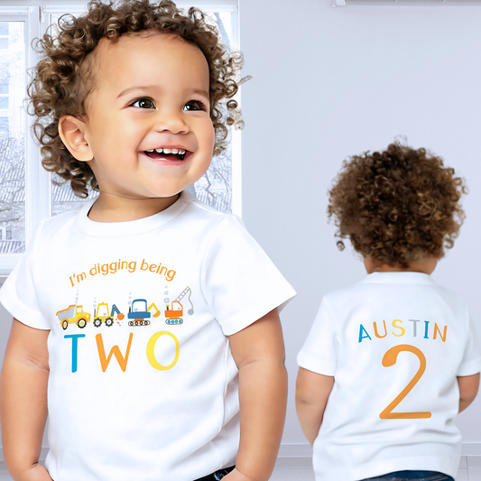 Personalised Excavator Boys Digger Birthday T-Shirt: This white t-shirt features a vibrant yellow tractor graphic alongside the playful text “I am digging being” with customisable age options to celebrate a birthday. The back is personalised with the boys name and age in vibrant yellow, blue and orange to match the digger theme. Ideal as a gift for a boy or toddler birthday or a construction-themed party, boys birthday gift, toddler birthday tshirt with printed back, personalised tractor shirt