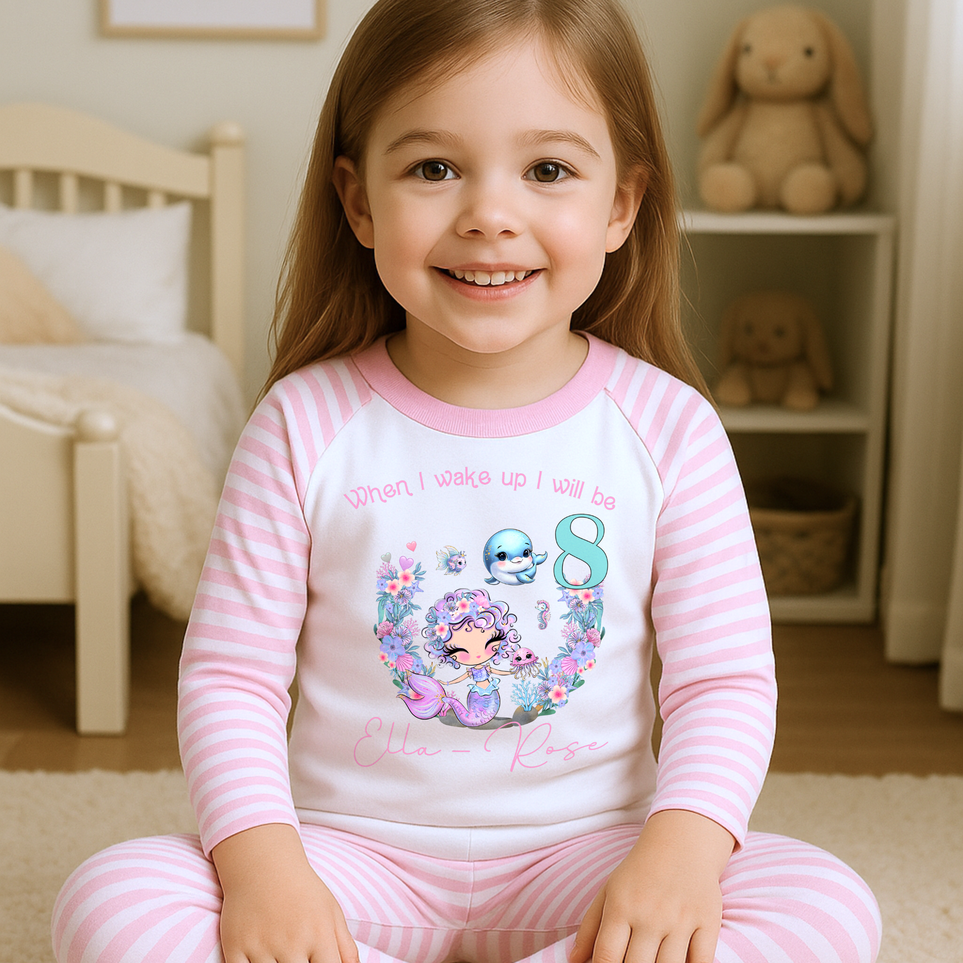 Mermaid birthday pyjamas, personalised for girls: A pair of mermaid birthday pyjamas in lilac and pink, featuring a glitter-like design. The top displays the phrase “When I Wake Up I Will be,” personalized with a girl's name and age. Ideal for young mermaid enthusiasts, these Pyjamas make a magical birthday gift for girls, when i wake up mermaid