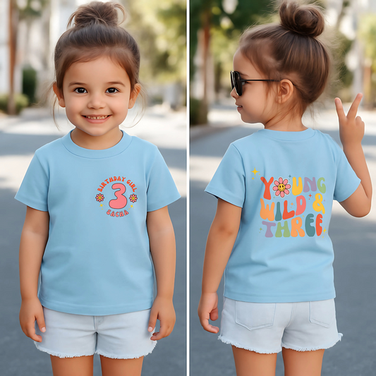 Young Wild and three birthday t-shirt: A girls' birthday T-shirt with a "Young Wild and Three" theme, showcasing a groovy retro style. The front features whimsical retro emojis and the words "birthday girl" alongside a customisable name on the left breast. The back displays bold retro fonts and graphics for a nostalgic touch. Made from soft, high-quality fabric, this vibrant and playful tee is designed for comfort and style, perfect for third birthdays.