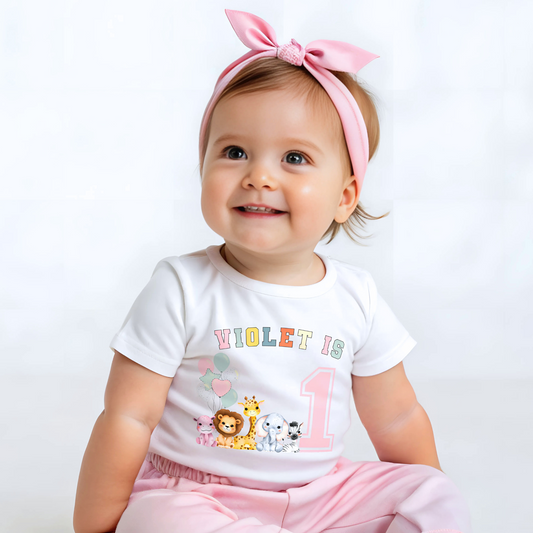 Animal birthday t-shirt, A white t-shirt featuring a vibrant graphic with pink, sage, and neutral tones, showcasing a personalized "Birthday Girl" design. The graphic includes the girl's name and an age-representing number. It incorporates a lively safari jungle animal theme adorned with colorful birthday balloons. This t-shirt makes an ideal birthday gift for a toddler safari-themed birthday party celebration, adding a personalized touch to the festivities.