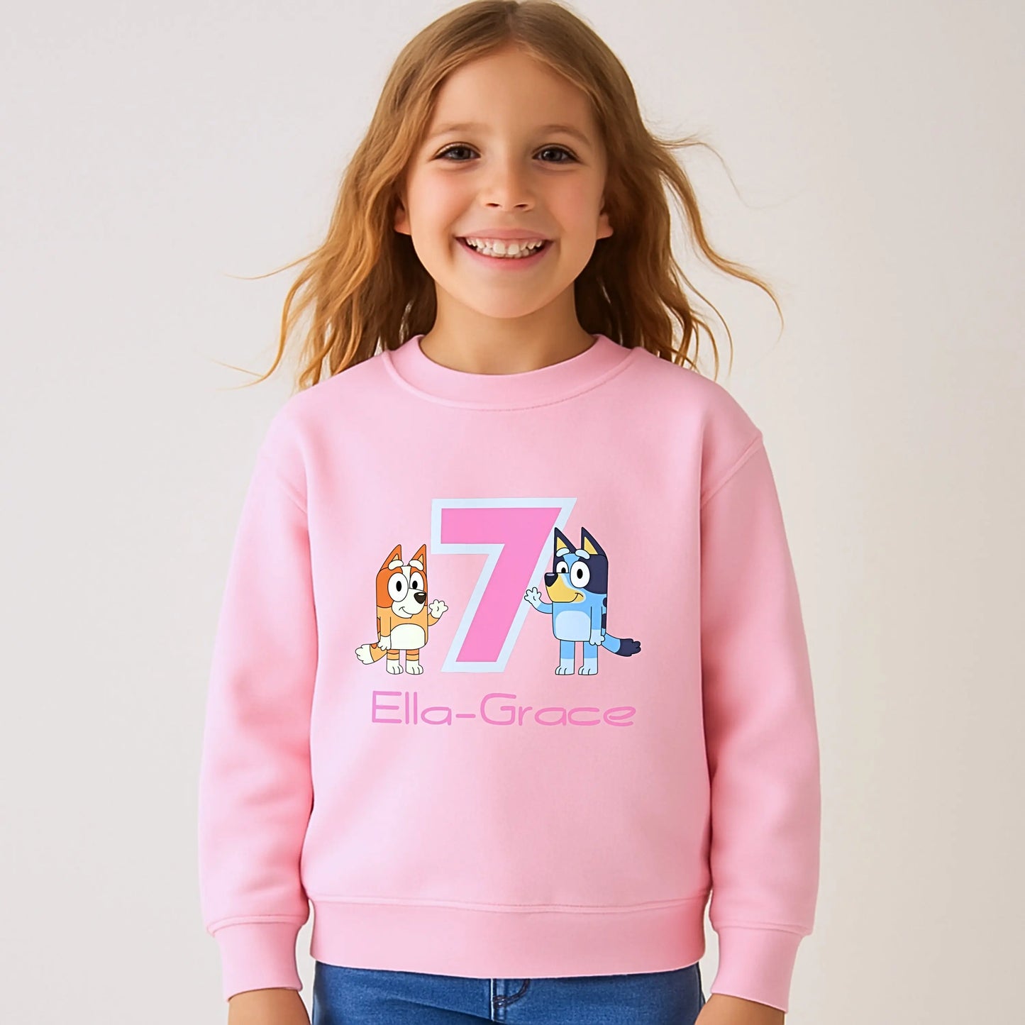 Persoalised Bluey and Bingo birthday sweatshirt: Child wearing a purple sweatshirt with bluey and bingo characters and her name underneath