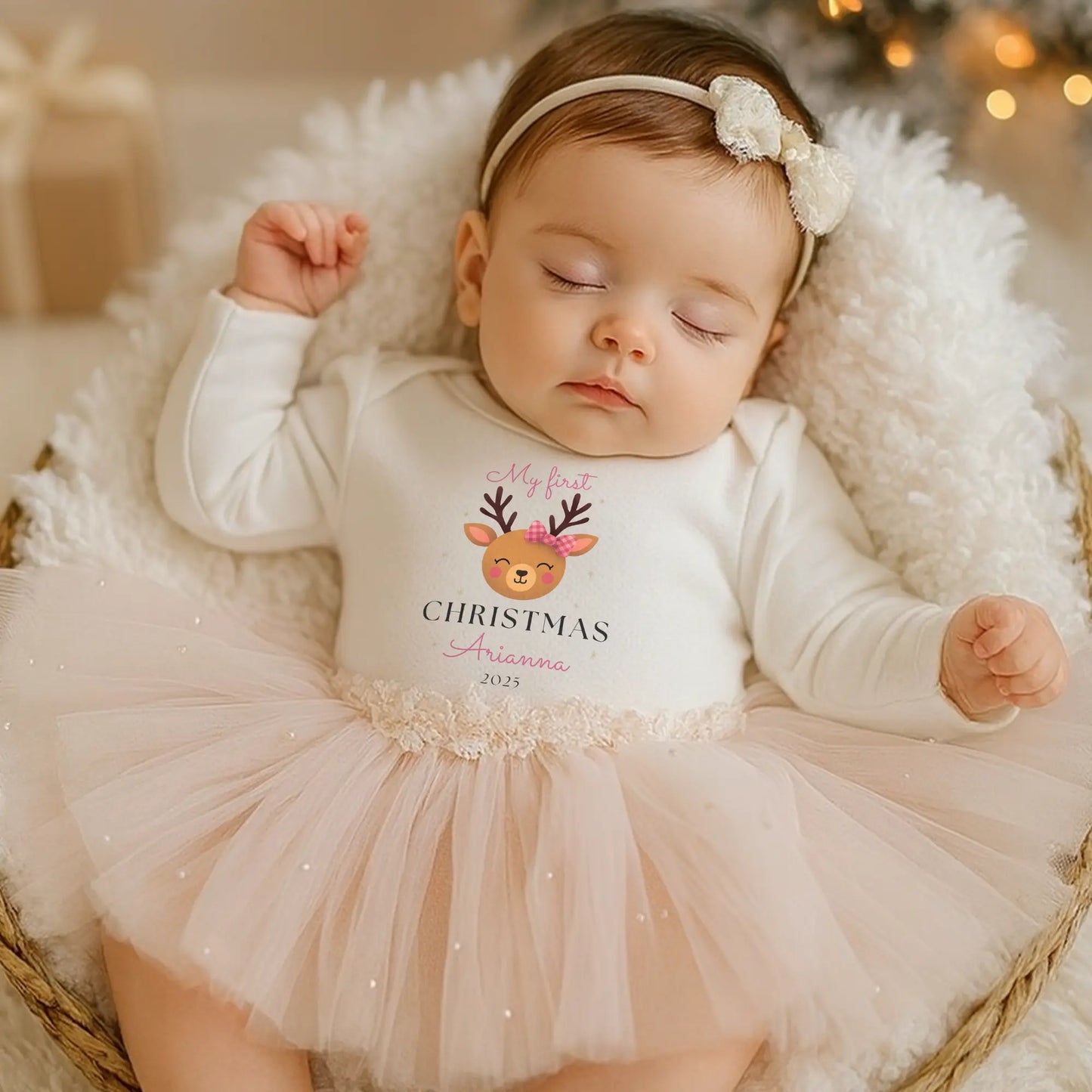 Baby Girl’s 1st Christmas Outfit: Baby girl in a personalisewhite onesie with a Christmas design, wearing a pink tutu and headband, surrounded by festive decorations. 