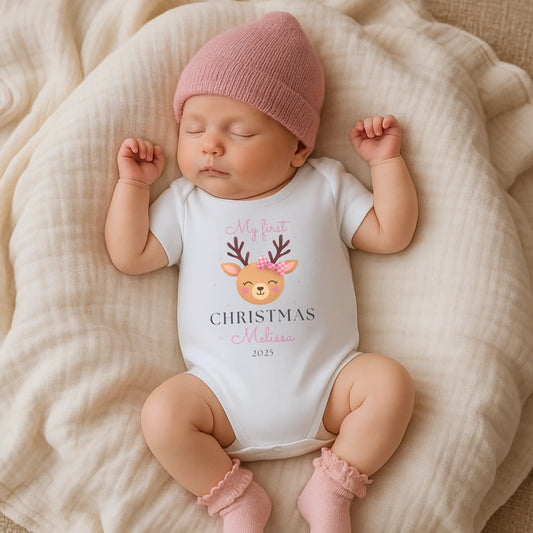 Baby Girl’s 1st Christmas Outfit: Newborn baby wearing a personalised white onesie with a Christmas design and pink hat, lying on a soft surface.