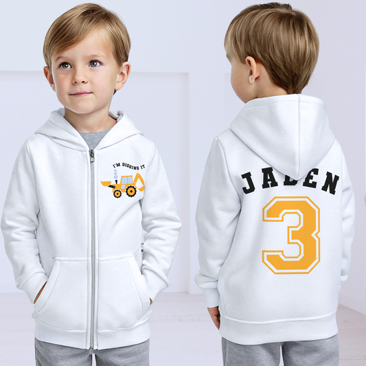 Boys Digger Hoodie: kids personalised zip-up hoodie featuring a playful construction theme. The back of the hoodie showcases the childs name and number in a varsity font. On the front is a vibrant print of a digger or tractor with the words I am Digging it, adding a fun touch for young construction enthusiasts. Great for toddler birthday gifts, graphic hoodie for boys, birthday gift, Name and Number Hoodie for Kids.