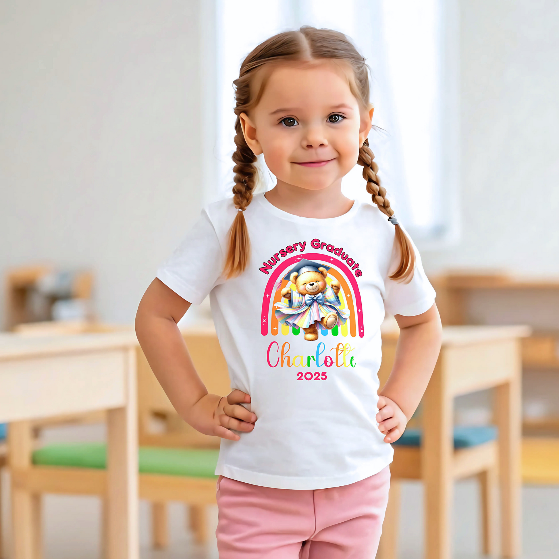 A girl wearing a white Personalised Nursery Leavers T-shirt. Above the rainbow it says Nursery Graduate and below it is a girl bear in graduation clothes on soft fluffy clouds. Below the design is the girls name and year of graduation.