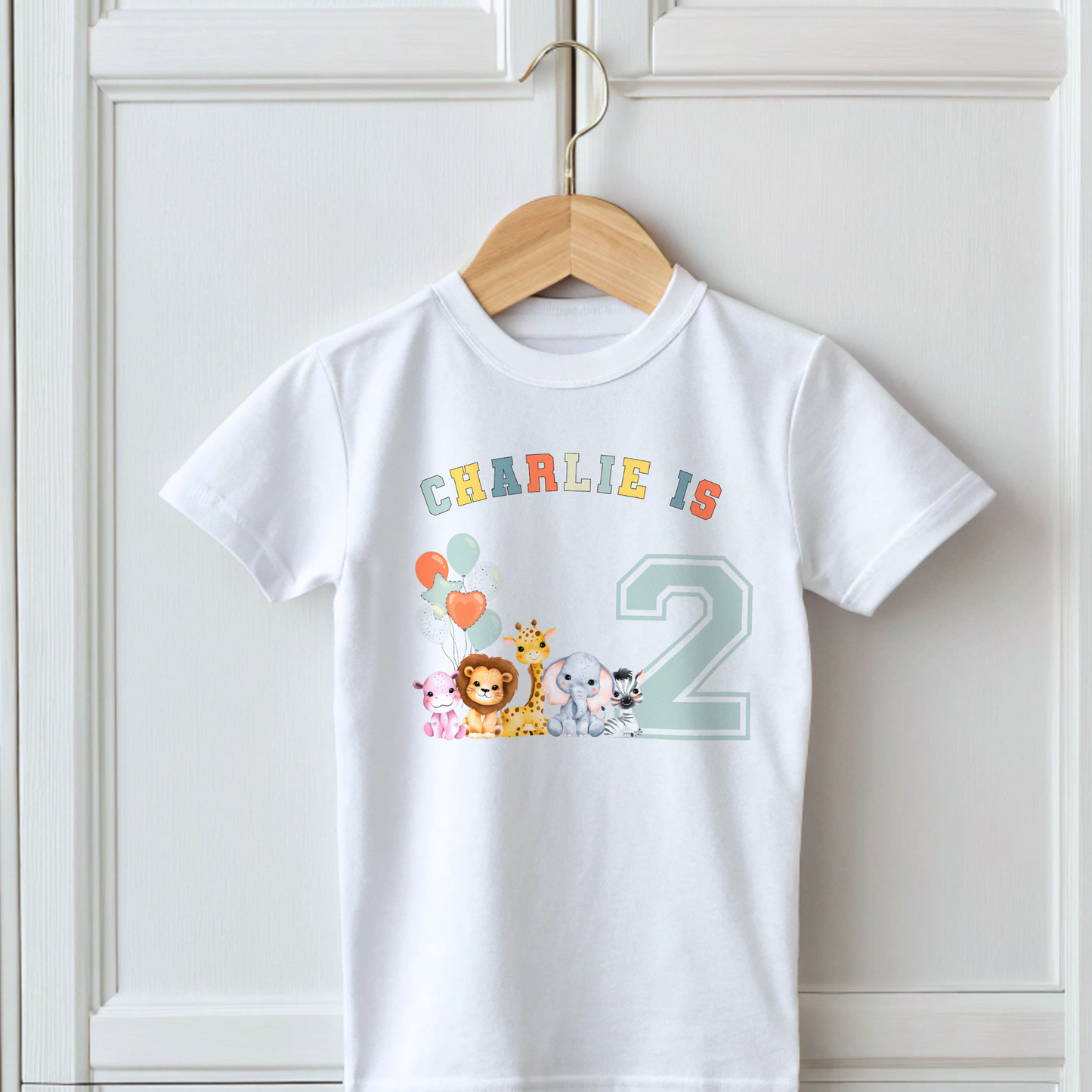 Animal birthday t-shirt, A white t-shirt featuring a vibrant graphic with sage, and neutral tones, showcasing a personalized birthday boy design. The graphic includes the boys name and an age-representing number. It incorporates a lively safari jungle animal theme adorned with colourful birthday balloons. This t-shirt makes an ideal birthday gift for a toddler safari-themed birthday party celebration, adding a personalised touch to the festivities.
