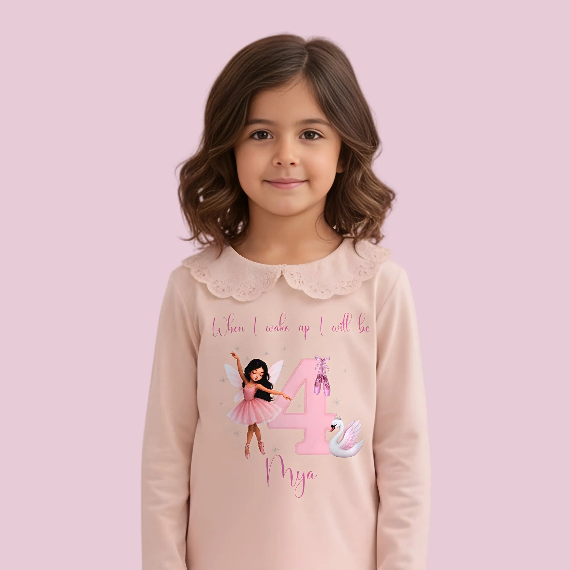 Ballerina Birthday Pyjamas - Young girl wearing a pink outfit with a fairy design and text, sitting on a carpeted floor.