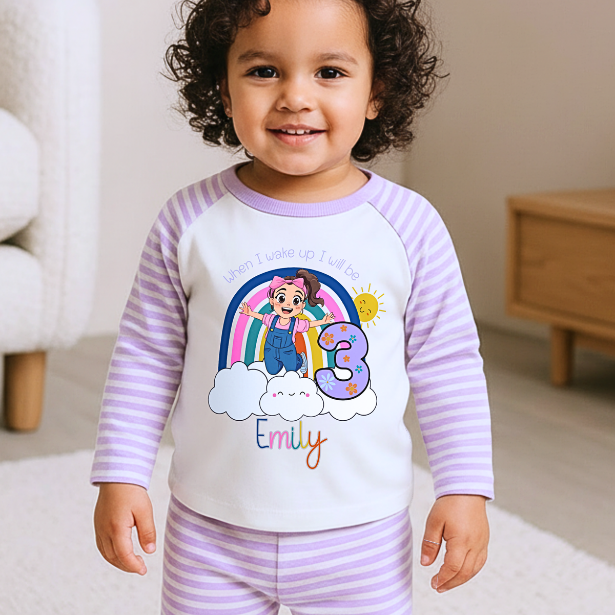 Personalised Ms Rachel Birthday PJs for Girls, When I Wake up Ms Rachel Pyjamas AishaBaileyDesigns: A smiling toddler wearing a custom pajama set with lavender and white stripes, featuring a white front panel with a colorful cartoon rainbow, character, the number 3, and the name 'Emily'.