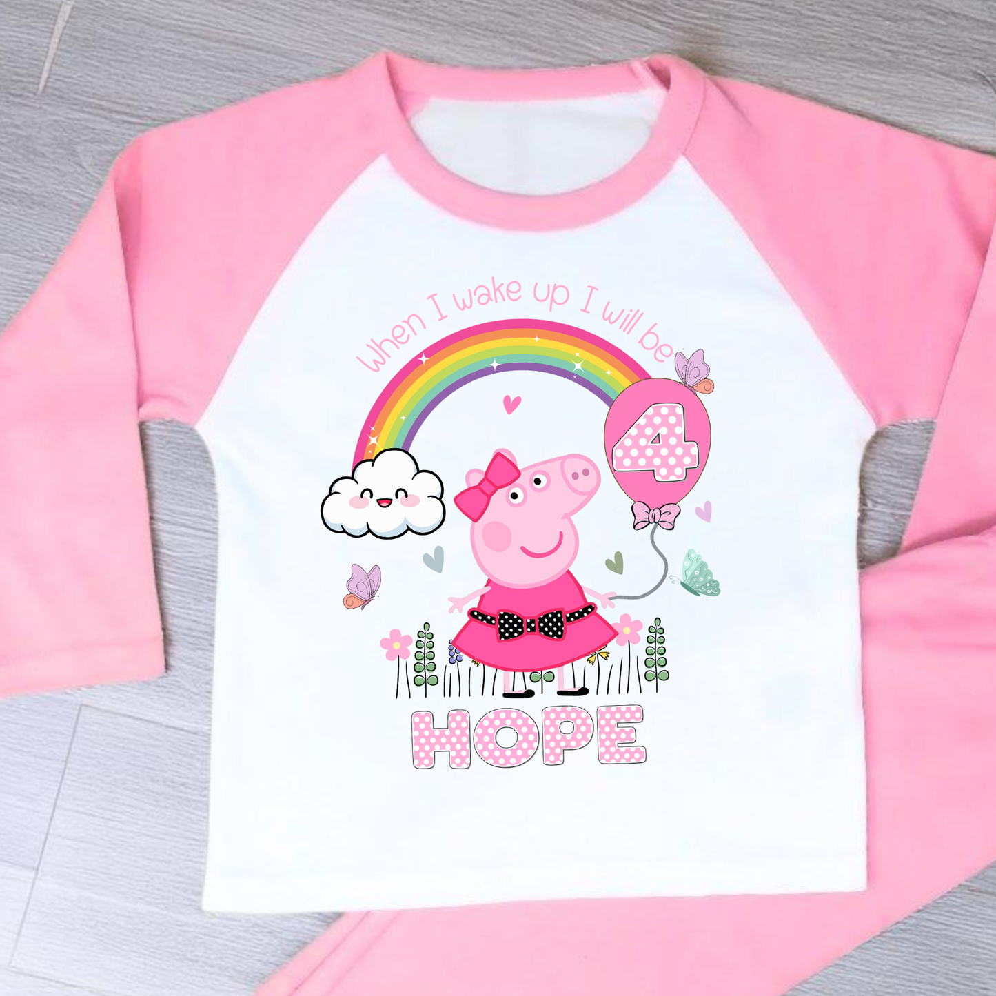 Peppa Pig birthday pyjamas: set of Personalised Peppa Pig Birthday Pyjamas designed for little girls, featuring Peppa Pig in a whimsical spring garden theme with blooming flowers and vibrant colours. The pyjamas include a playful rainbow with pink polka dots, displaying the child's age for a personalised touch. The set is personalised with the child's name, making it a unique gift for Peppa Pig fans, perfect for wearing on the eve of their birthday.