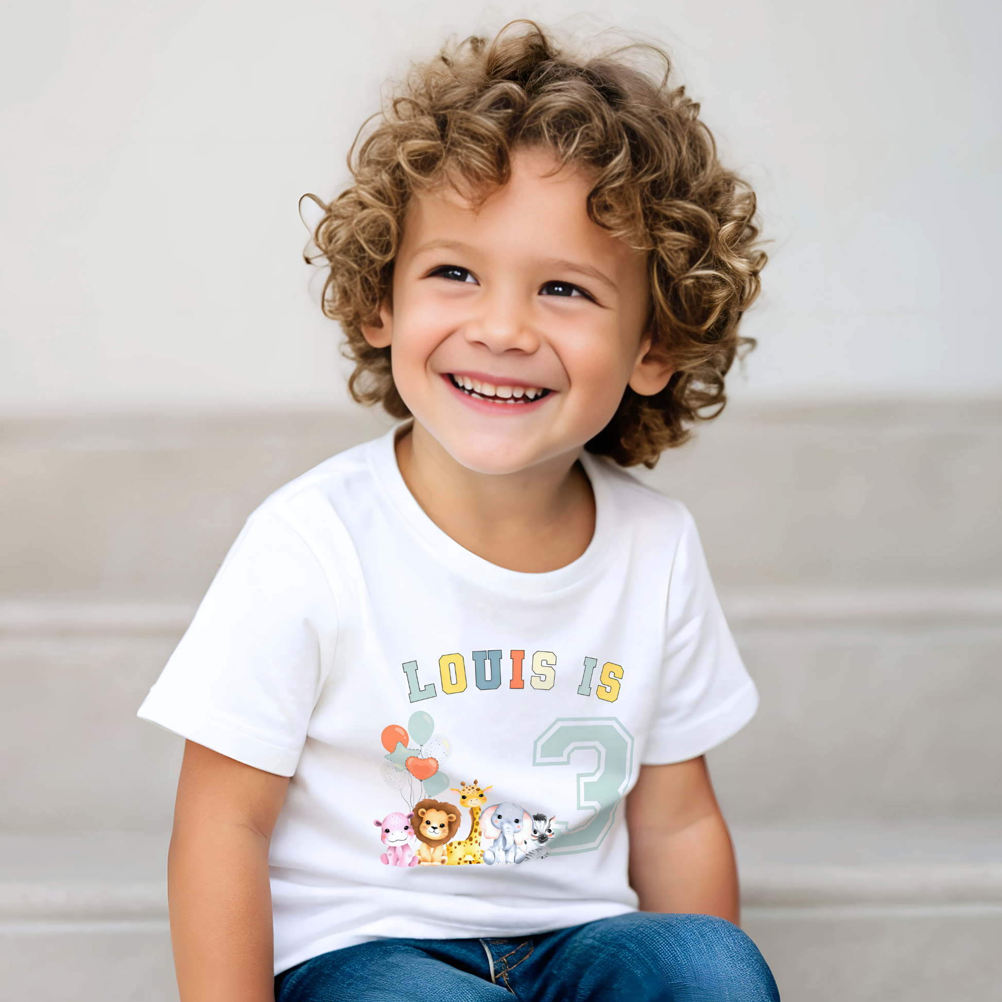 Animal birthday t-shirt, A white t-shirt featuring a vibrant graphic with sage, and neutral tones, showcasing a personalized birthday boy design. The graphic includes the boys name and an age-representing number. It incorporates a lively safari jungle animal theme adorned with colourful birthday balloons. This t-shirt makes an ideal birthday gift for a toddler safari-themed birthday party celebration, adding a personalised touch to the festivities.