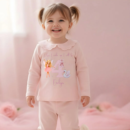 Ballerina Birthday Pyjamas - Young girl wearing a pink outfit with a fairy design and text, sitting on a carpeted floor.