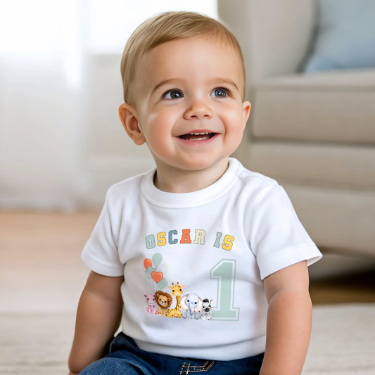 Animal birthday t-shirt, A white t-shirt featuring a vibrant graphic with sage, and neutral tones, showcasing a personalized birthday boy design. The graphic includes the boys name and an age-representing number. It incorporates a lively safari jungle animal theme adorned with colourful birthday balloons. This t-shirt makes an ideal birthday gift for a toddler safari-themed birthday party celebration, adding a personalised touch to the festivities.