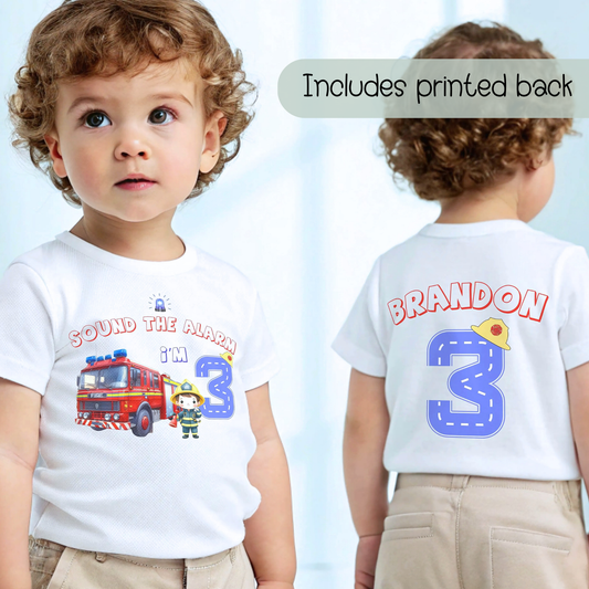 Personalised Fire Engine Birthday T-Shirt: A customizable white birthday shirt featuring a red fire truck and firefighter. The top reads “Sound the Alarm I'm” followed by your choice of age number. The back displays the toddler's name and a blue number adorned with a firefighter hat. An ideal gift for firefighter-themed birthday parties for toddlers.