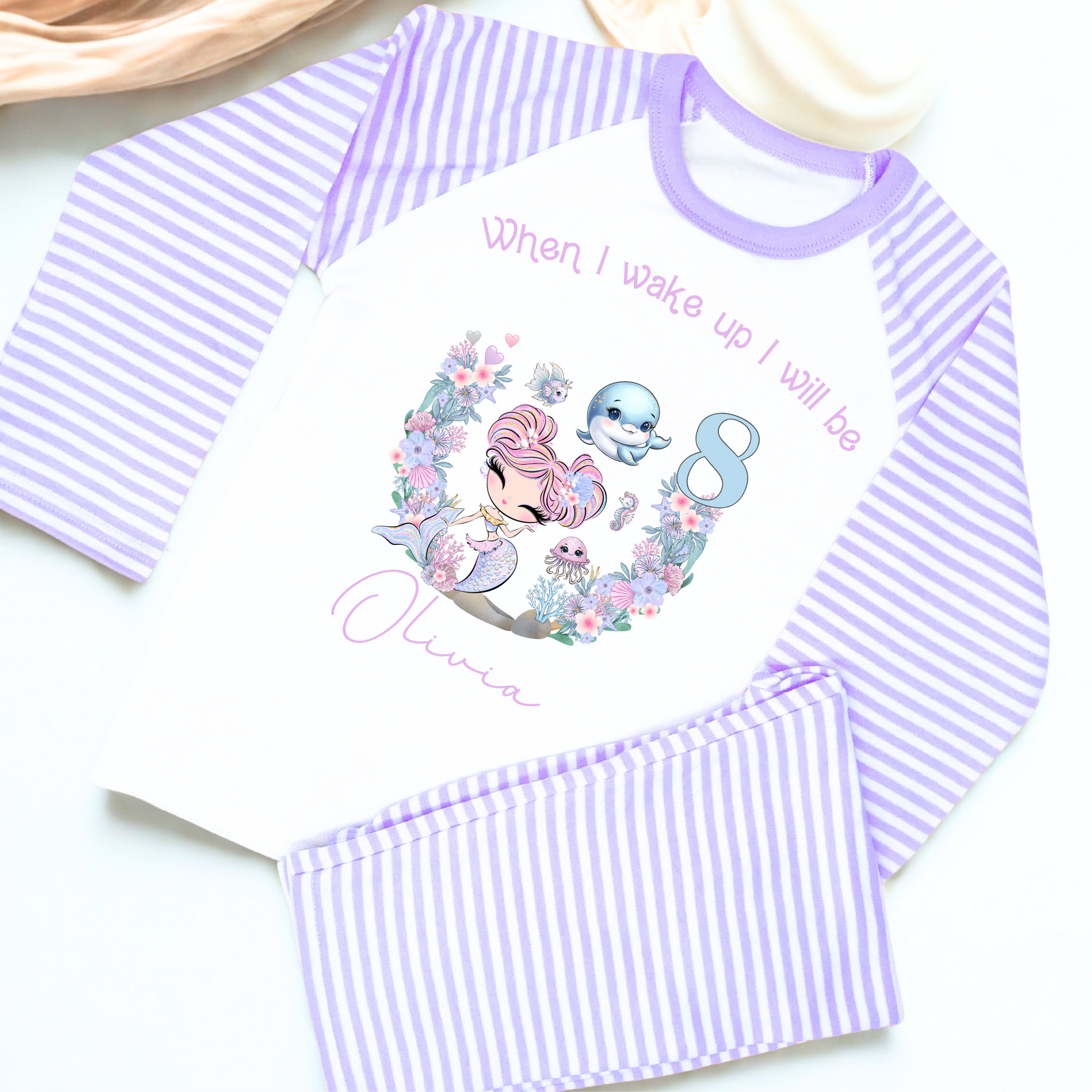 Mermaid birthday pyjamas, personalised for girls: A pair of mermaid birthday pyjamas in lilac and pink, featuring a glitter-like design. The top displays the phrase “When I Wake Up I Will be,” personalized with a girl's name and age. Ideal for young mermaid enthusiasts, these Pyjamas make a magical birthday gift for girls, when i wake up mermaid