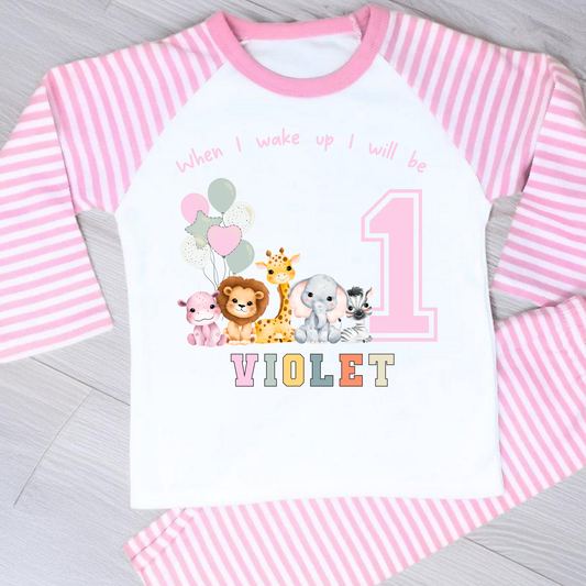 safari birthday pyjamas, A personalised set of girls birthday pyjamas in pink. At the top it says when i wake up i will be followed by some safari jungle animals holding some birthday balloons. They are sat beside a number that represents the child age on birthday. Under that is the child name in safari rainbow colours. This is perfect gift for a toddler first birthday.