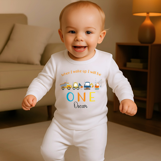 Personalised First Birthday pyjamas: personalised set of baby boy pyjamas for a first birthday,with a construction theme. The pyjamas display a playful design with diggers and excavators. The top reads: When I Wake Up I’ll Be ONE incorporating the child&#39;s name for a personalised touch. This set is ideal for toddlers who love construction vehicles, offering both comfort and a fun, imaginative theme: personalised baby pyjamas, first birthday, digger, excavator, custom name, construction vehicles.